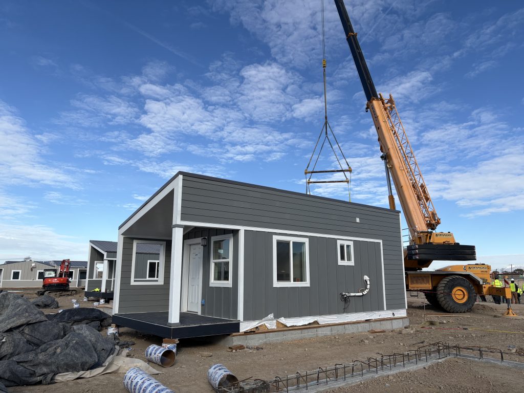 A tiny home placed in The Other Side Village with construction equipment in the background.