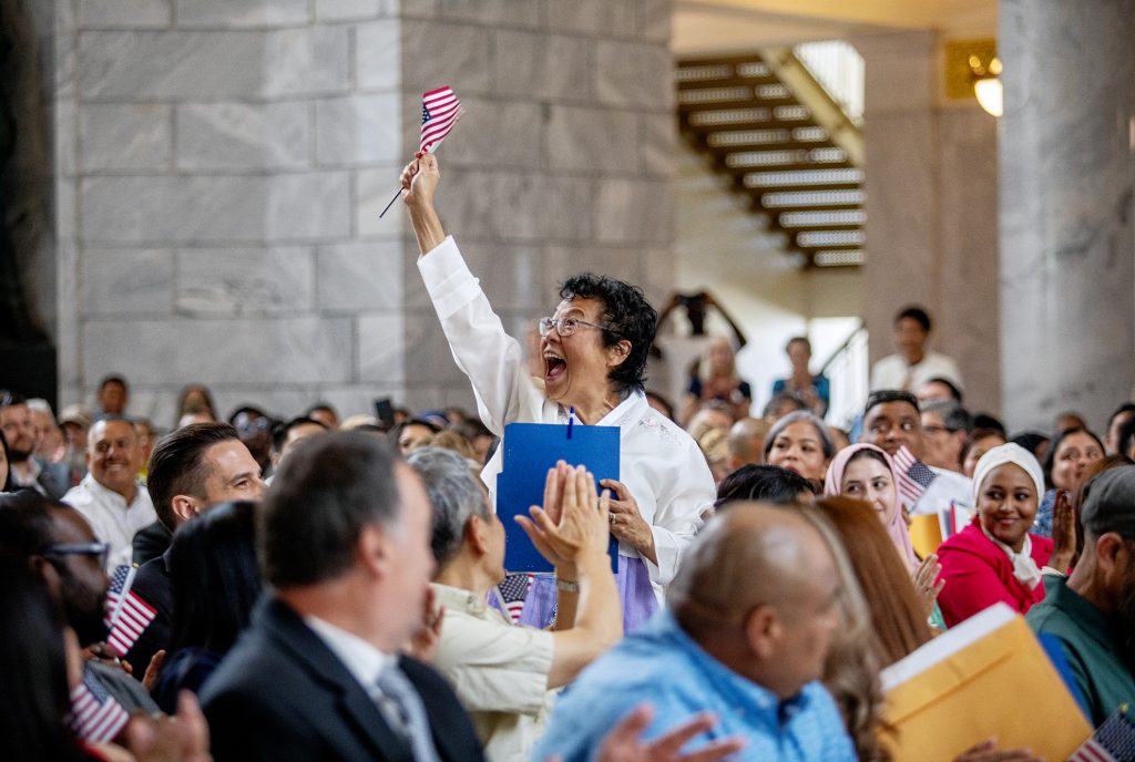 A woman holding a U.S. flag celebrates during a citizenship ceremony at the Utah Capitol building.