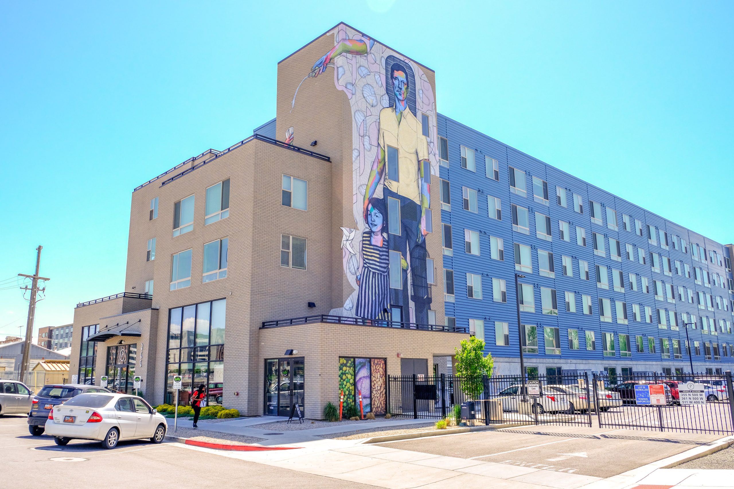 An apartment building on 500 W with a mural of a man and a young girl smiling. The words "Housing SLC" appear on top of the image. 