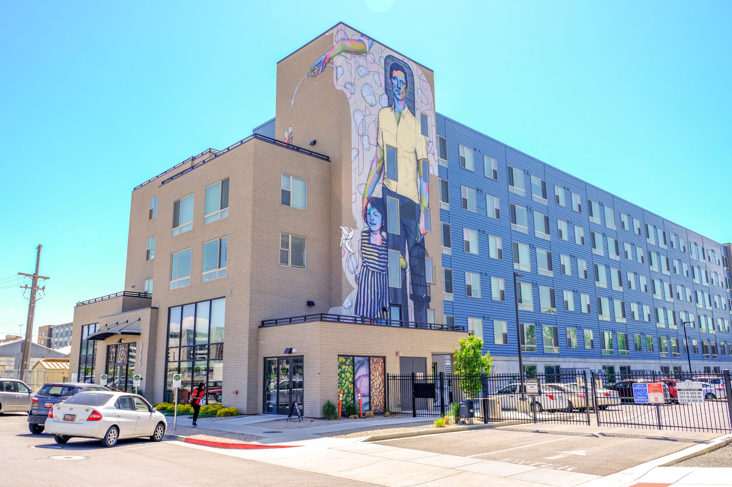 An apartment building on 500 W with a mural of a man and a young girl smiling. The words "Housing SLC" appear on top of the image.