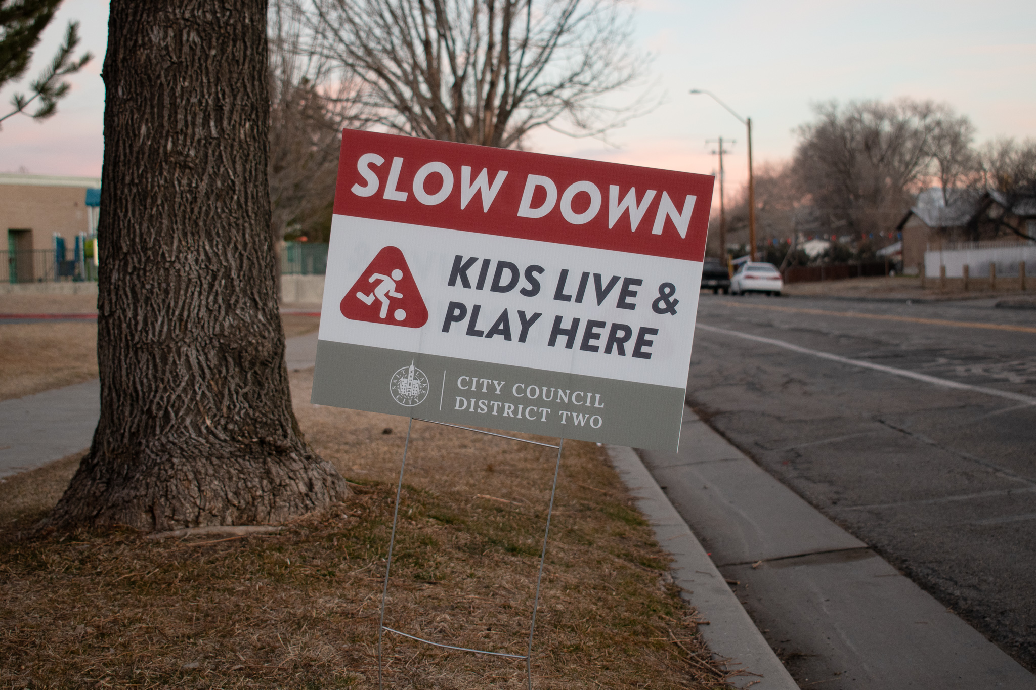 The traffic calming sign reads "Slow down. Kids live and play here. City Council District Two."