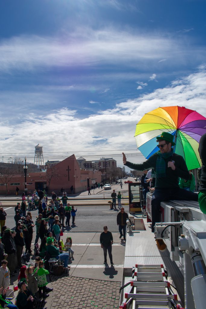 District 3 Council Member Chris Wharton waving at people watching the parade while he sits on the top of a fire truck.