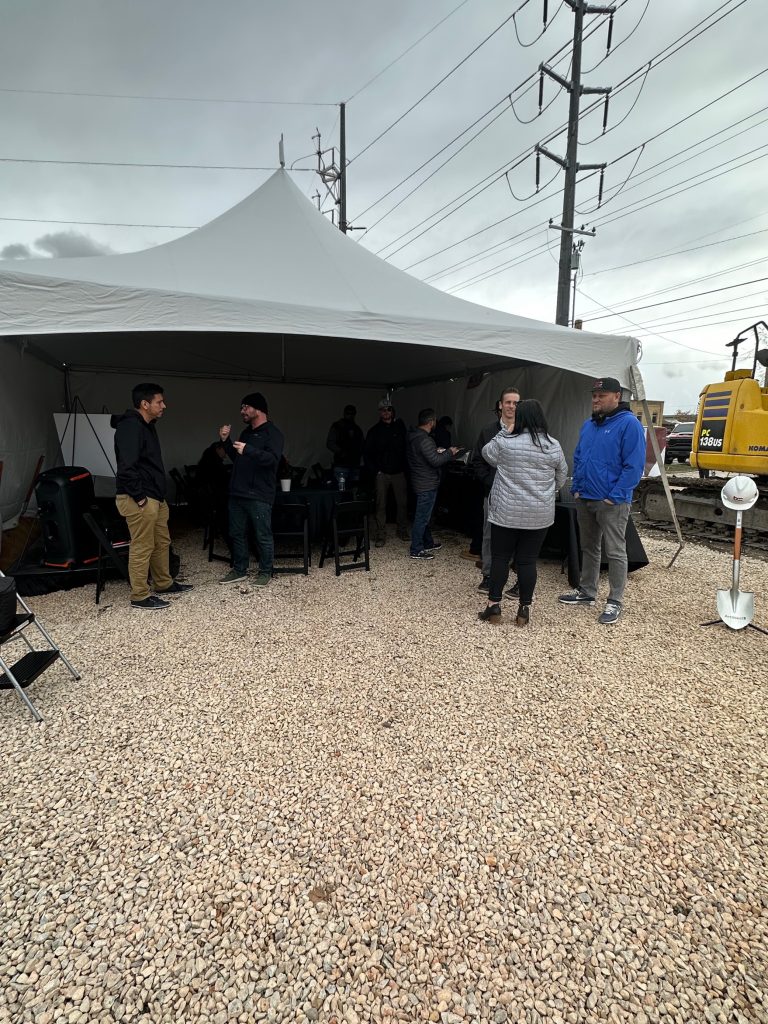 Attendees of the groundbreaking ceremony talking amongst themselves under a large tent.