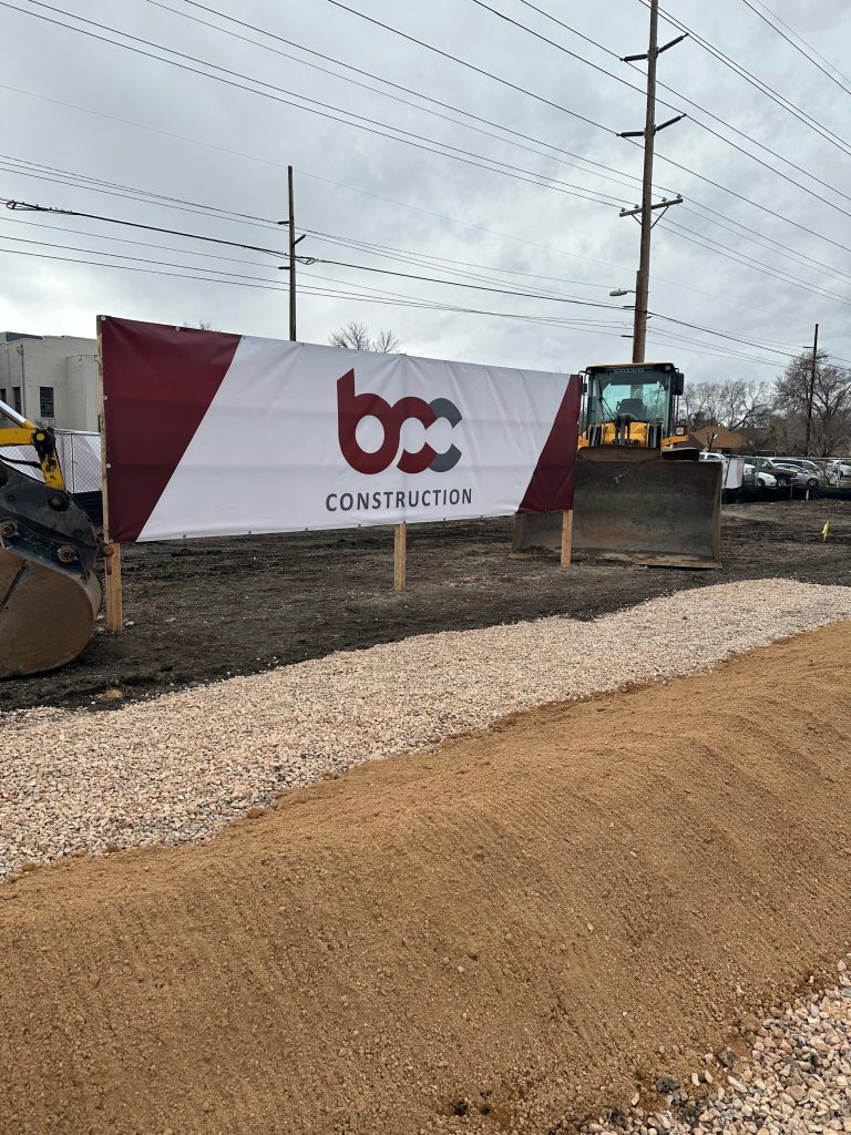 A large bcc construction banner set behind a large pile of dirt.