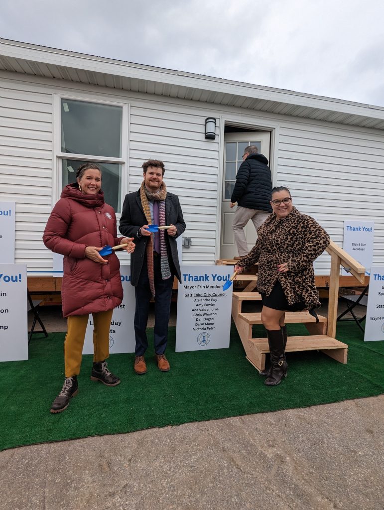 Salt Lake City Mayor Erin Mendenhall, District 1 Council Member Victoria Petro, and District 3 Council Member Chris Wharton posing in front of a tiny home at the groundbreaking ceremony.
