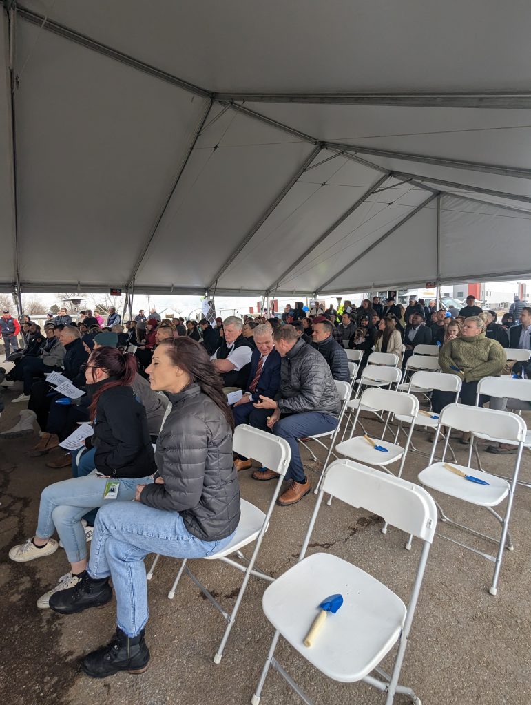 Crowd of attendees sitting under a tent at the Other Side Village Groundbreaking event.