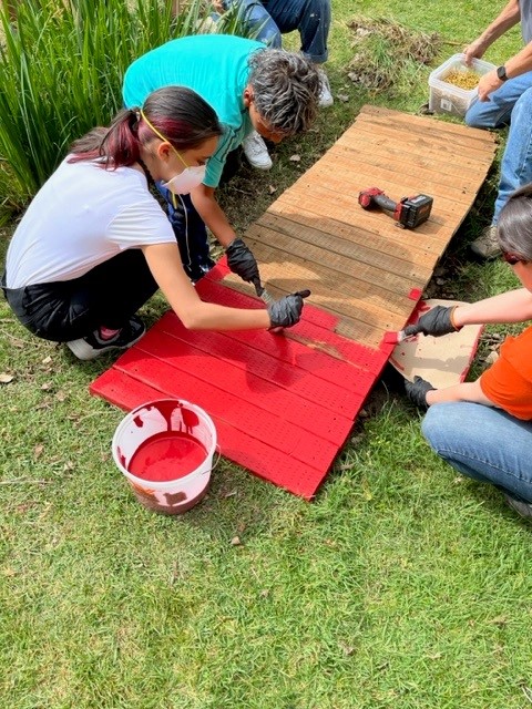 People painting a small bridge red.
