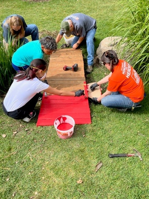 People painting a small bridge red.