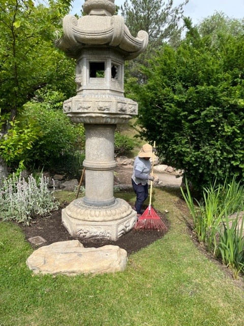 A woman raking the dirt around a tall Japanese statue.