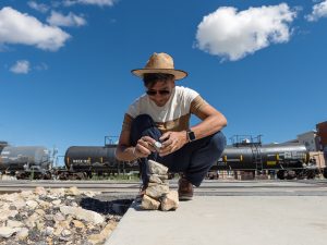 Alejandro Puy builds a rock cairn on the street in front of a train stopped at a crossing.