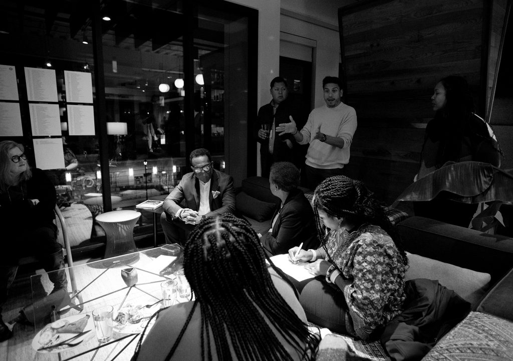 Balck and white image of Council Member Alejandro Puy speaking with eight people at the black history month annual community meeting.