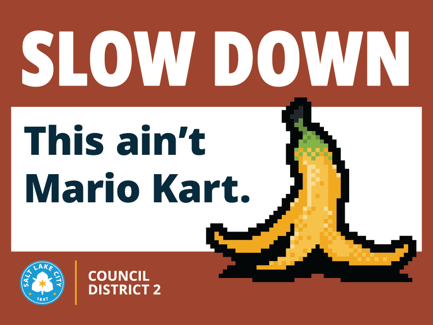 Sign with “SLOW DOWN. This ain’t Mario Kart.” and an illustrated pixel-style banana peel. Salt Lake City Council District 2.