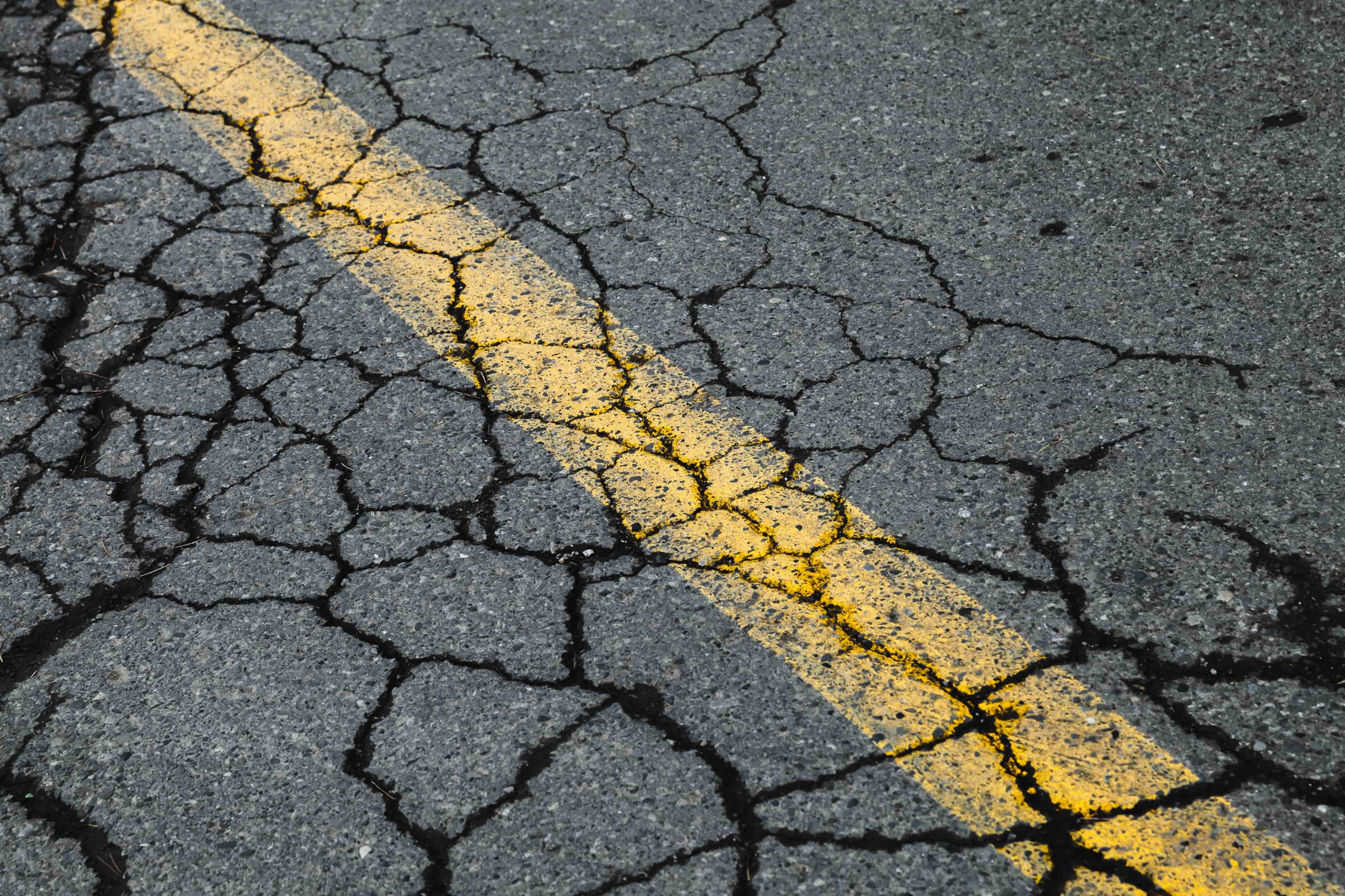 Cracked asphalt road with yellow dividing line.