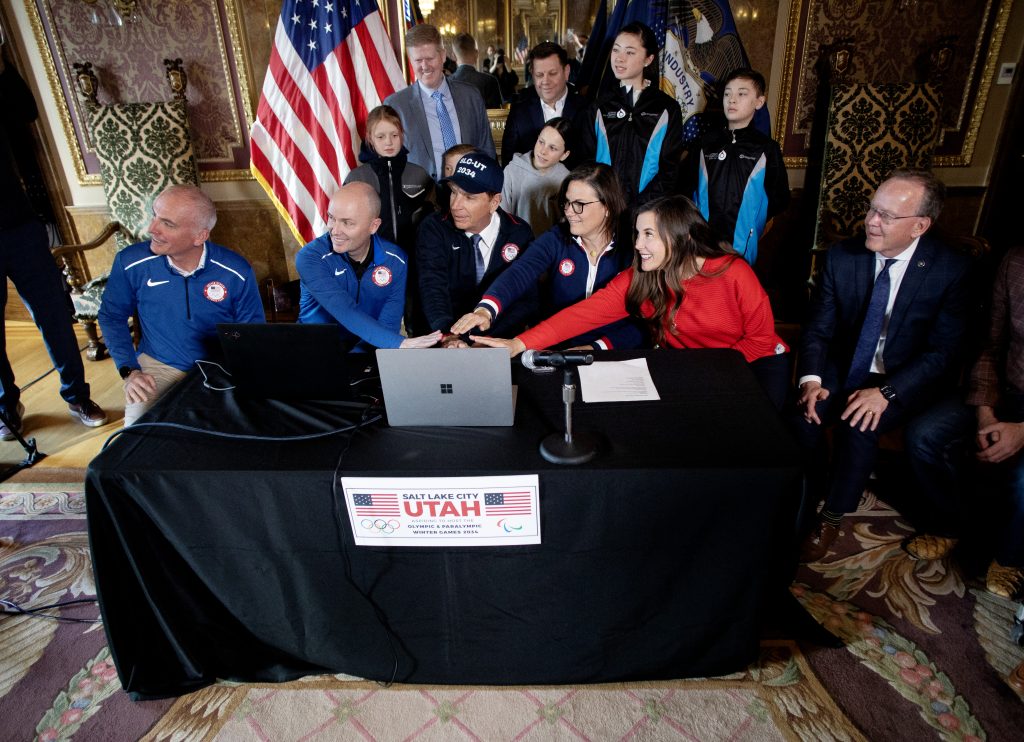 Members of the Salt Lake City-Utah Committee for the Games as well as Salt Lake City Mayor Erin Mendenhall (wearing red) and Utah Governor Spencer Cox (in light blue) press the button to submit a bid for the 2034 Olympic and Paralympic games. 
