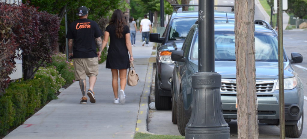People walking on the sidewalk next to cars parked in the street.