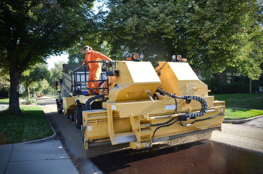 The chipper truck spreading chip onto a fresh surface of oil.