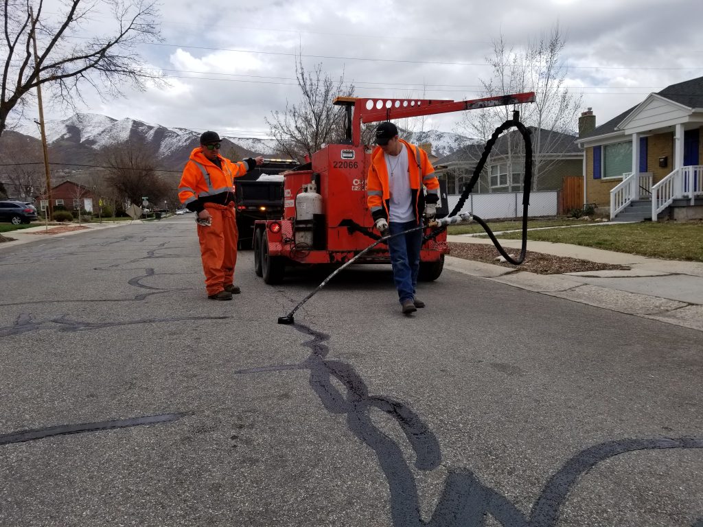 Two Salt Lake City Streets employees sealing cracks in a road.