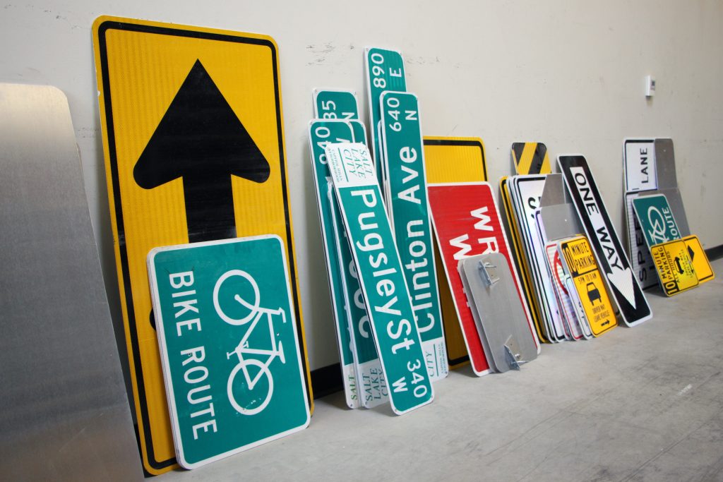 A variety of street signs laying against a wall.