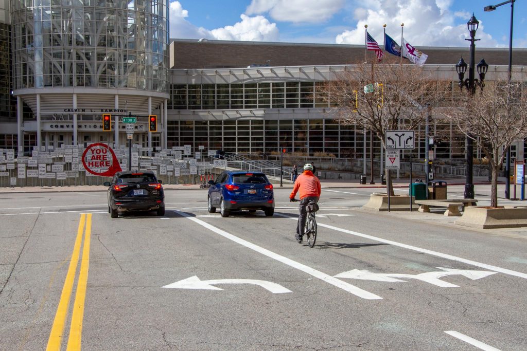 Two cars and a cyclist waiting to turn left onto West Temple at the 100 South traffic light