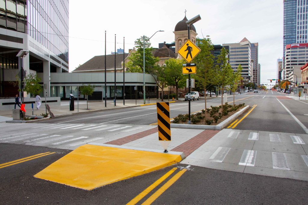 A picture of a crosswalk on 200 South, complete with flashing crosswalk signs and a landscaped pedestrian refuge island.