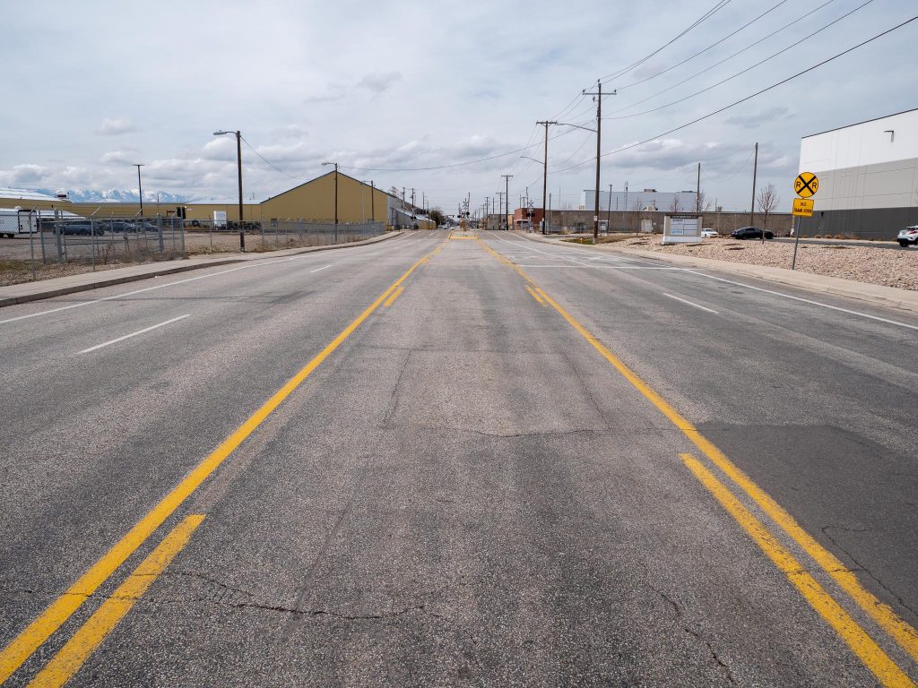 Existing conditions on 1700 South looking west at roughly 550 West. There are two travel lanes in each direction with a center two way left turn lane. There are also small painted bike lanes on the edges of the road in each direction.