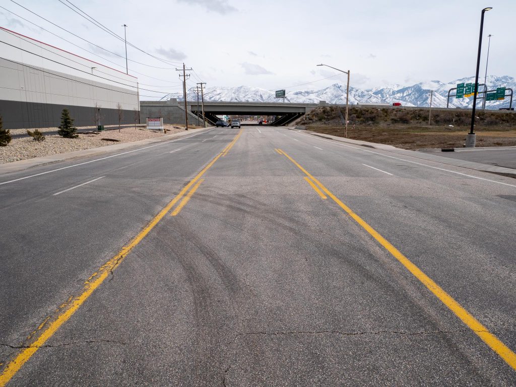 Existing conditions on 1700 South looking east at roughly 550 West. There are two travel lanes in each direction with a center two way left turn lane. There are also small painted bike lanes on the edges of the road in each direction. 