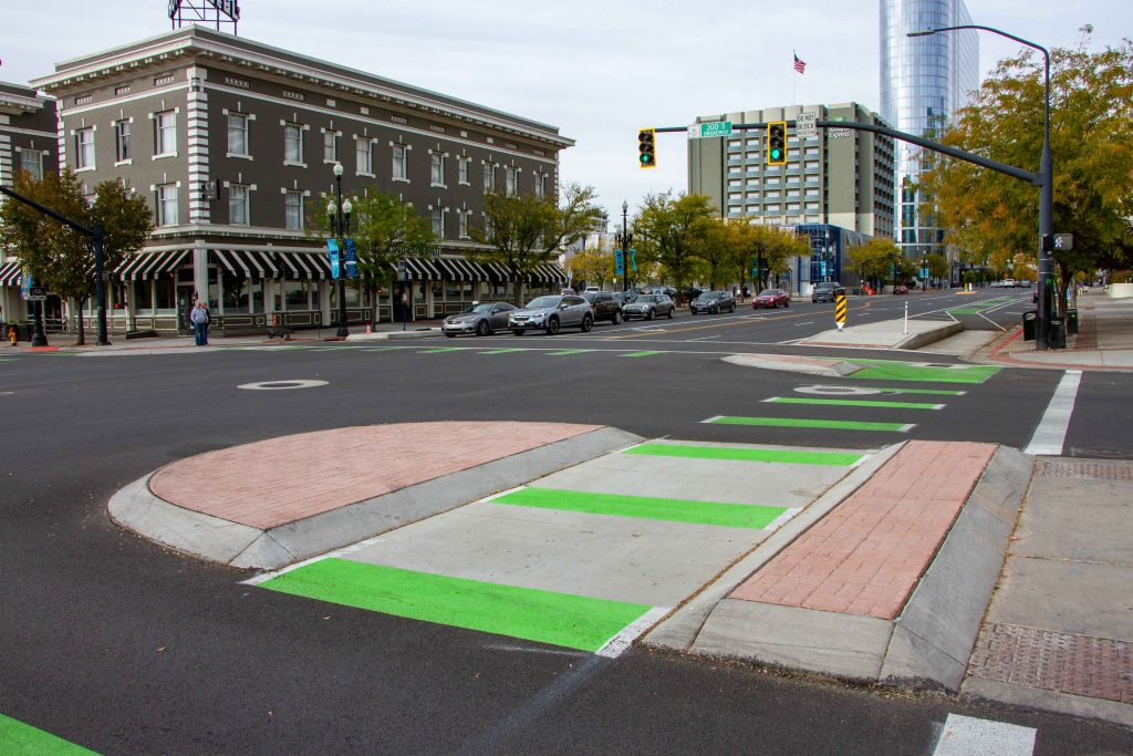 A picture of the intersection of 300 South and West Temple. There is a pedestrian refuge island and bright green crosswalk striping for cyclists.