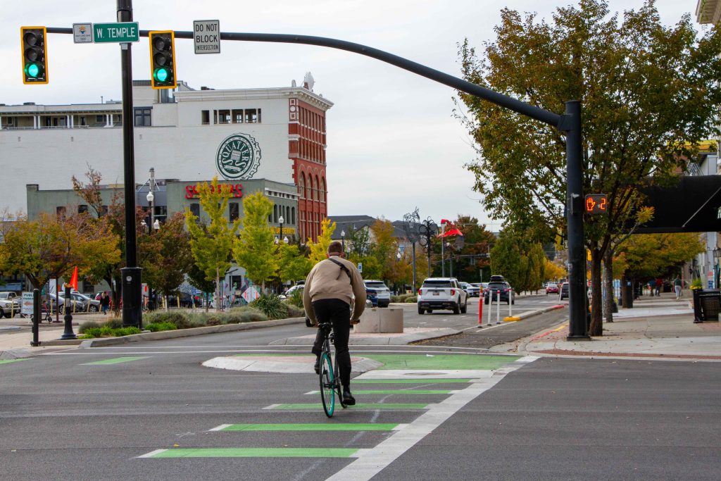 A picture of a person riding a bicycle through the intersection of 300 South and West Temple.
