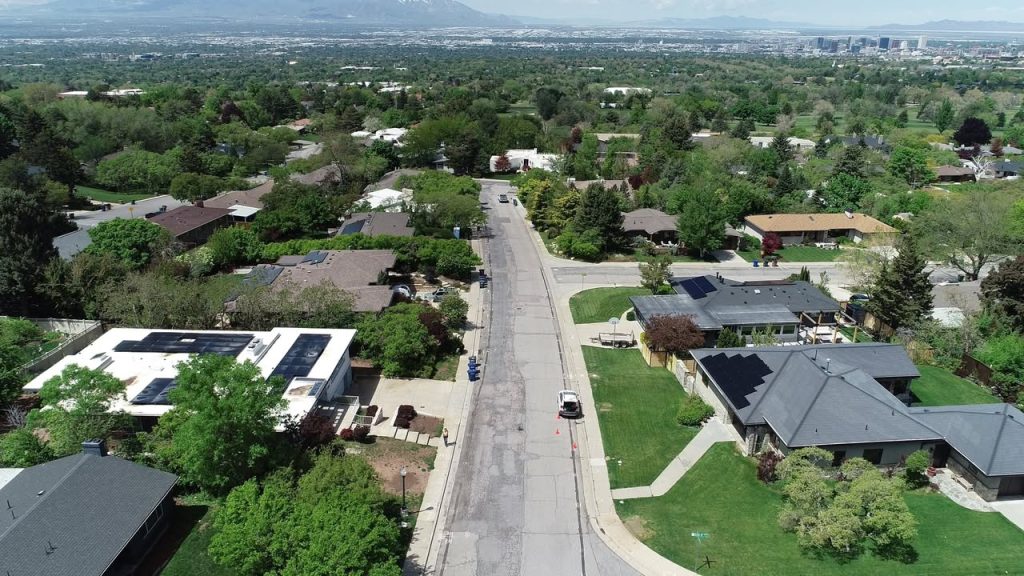 Aerial view of Oquirrh Drive in Salt Lake City before reconstruction, showing an older residential street with cracked pavement, mature trees, and single-family homes on both sides.