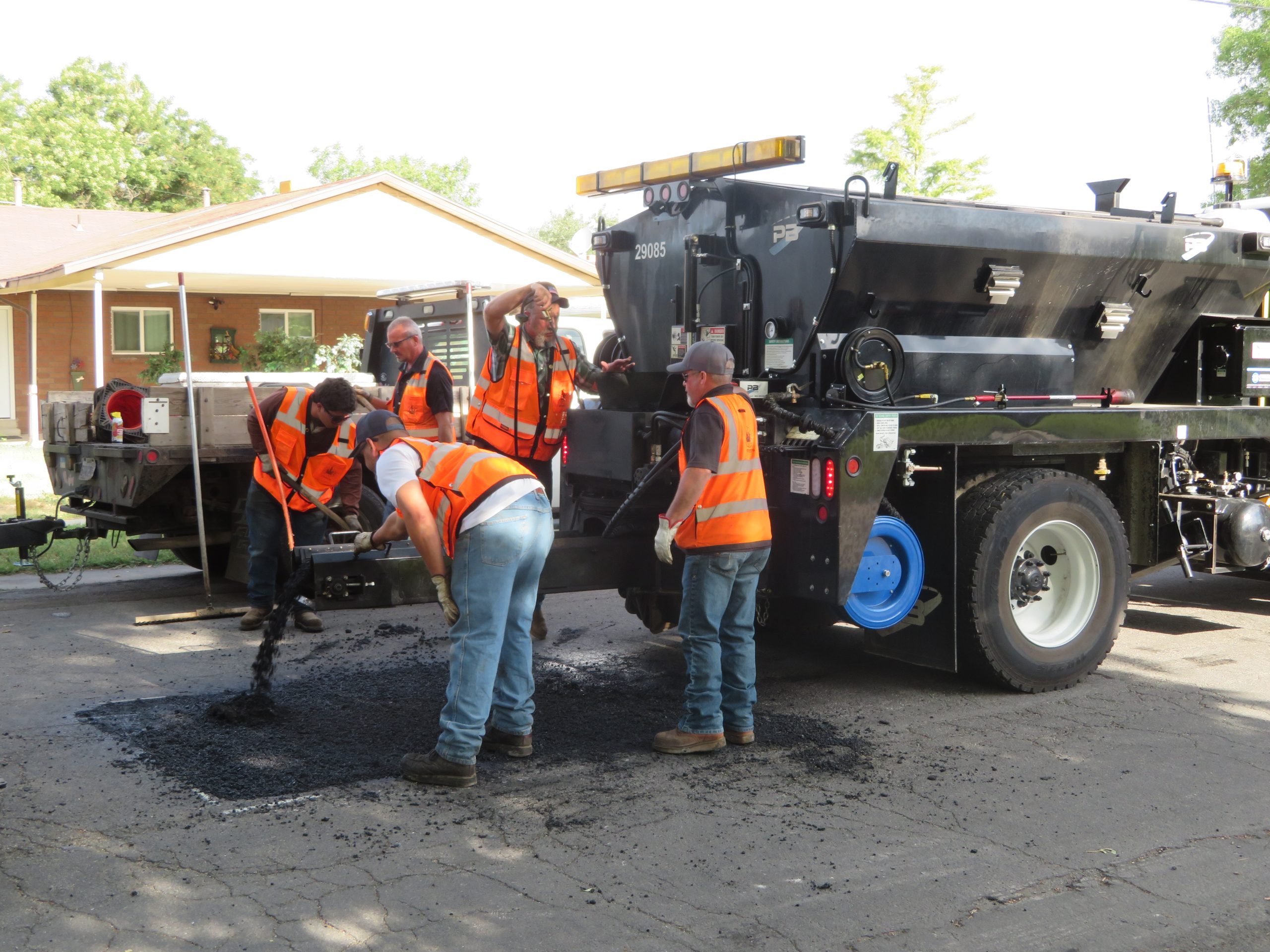 The patch truck adding oil and new asphalt to the reclaimed asphalt to mix, which is then rolled over to smooth out the repair