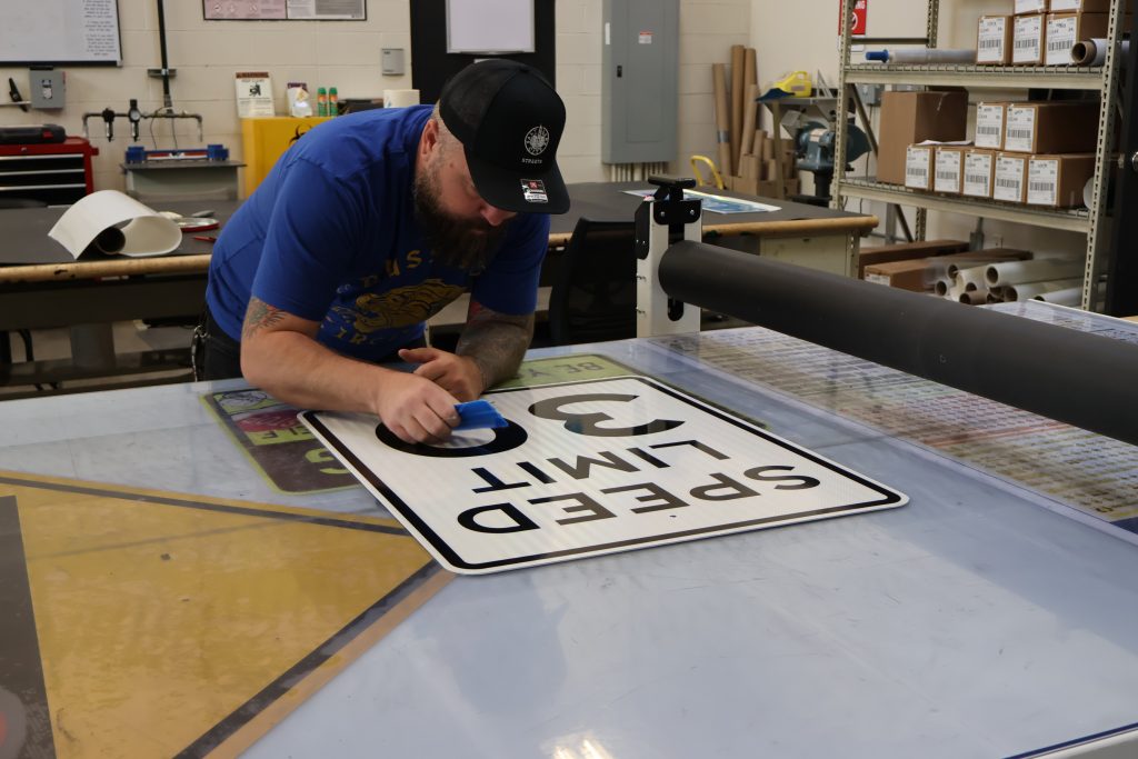 A Streets employee working air bubbles out of the vinyl on a speed limit sign.