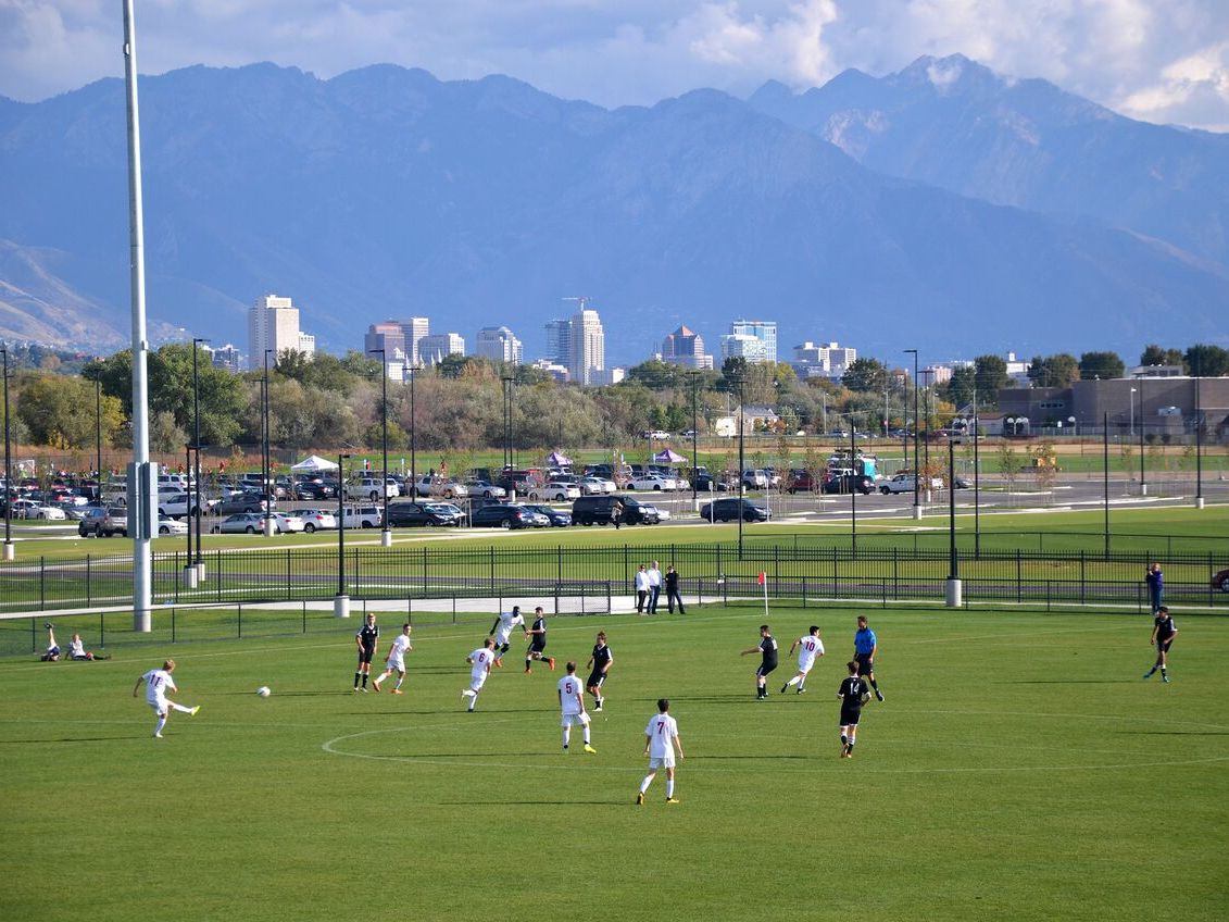 soccer players playing soccer on a field with city buildings and mountains in the back 