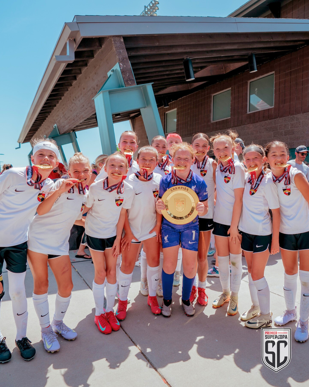 a children's soccer tyeam smiles. all are wearing medals and the child in the center holds a team award