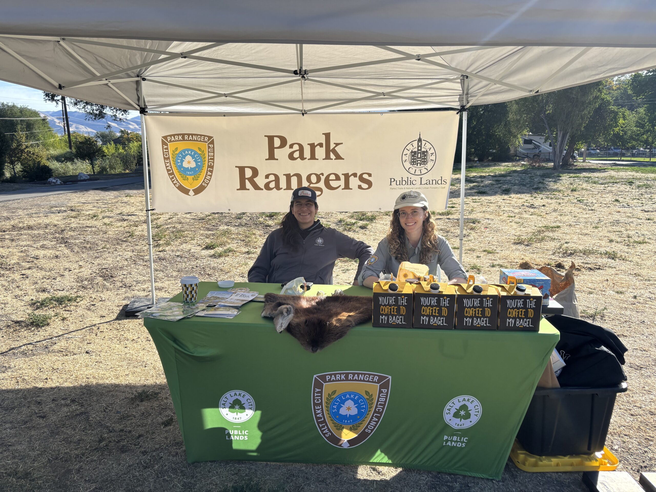 two park rangers smile and sit at a park ranger table with coffee 