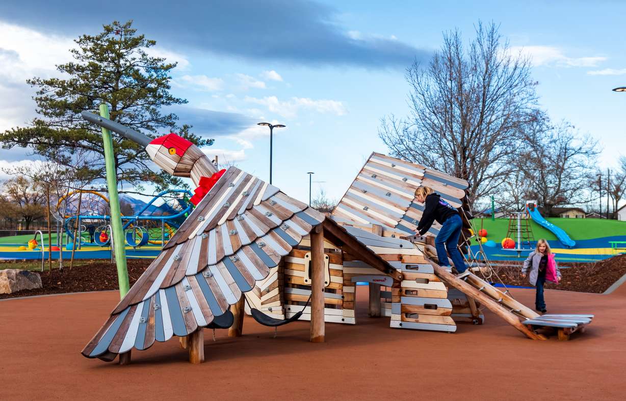 a wooden crane climbing structure in a park with a child climbing it.
