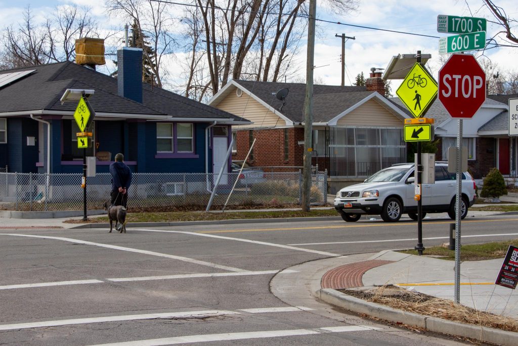 A person walking their dog across the crosswalk at 600 East and 1700 South.