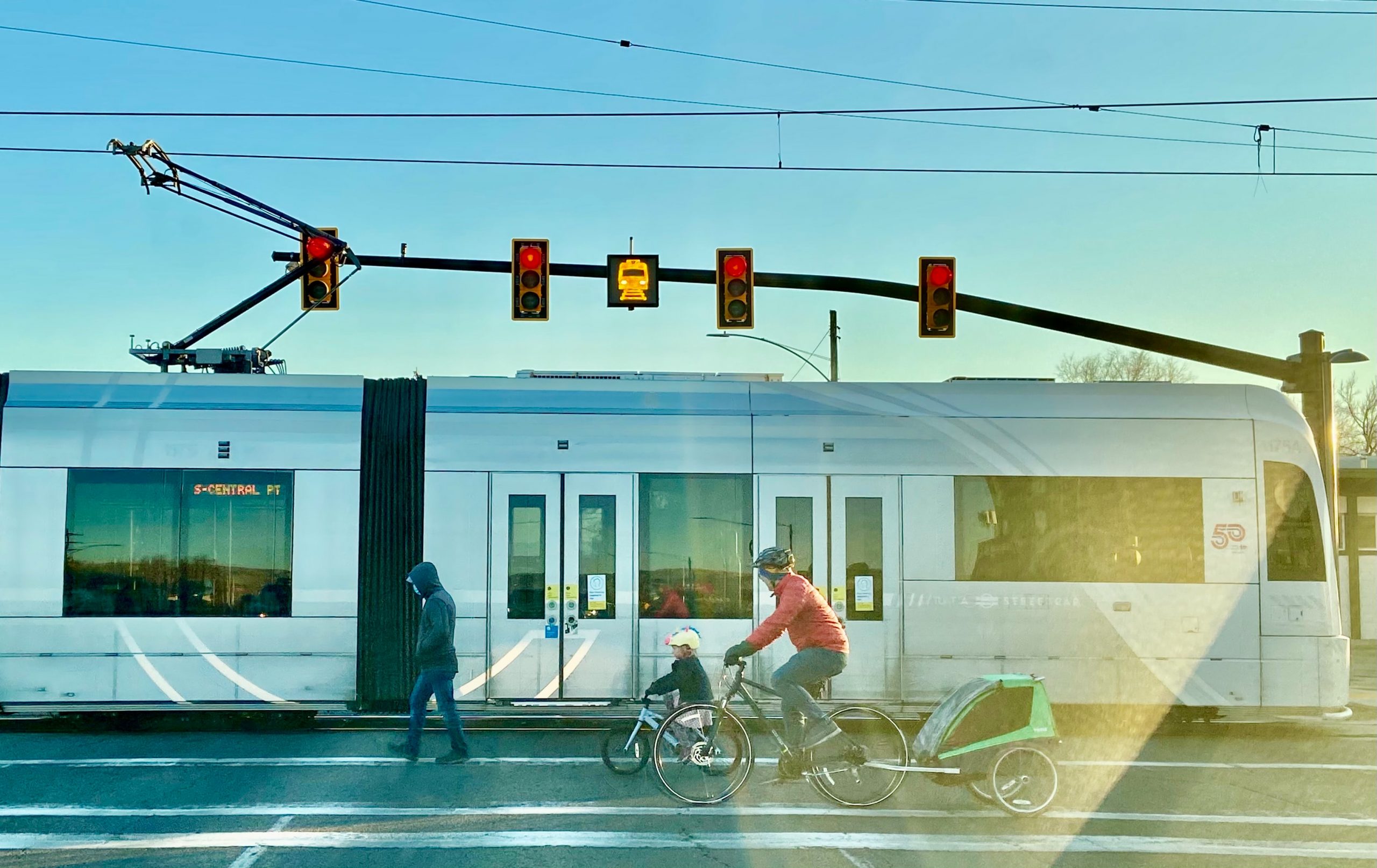 A picture of people walking and biking in the street with the S-Line streetcar passing by.