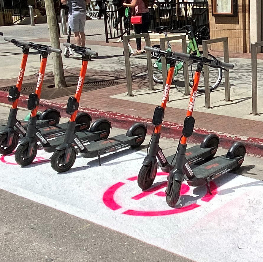 Row of scooters sitting in a freshly painted parking stall for Spin scooters