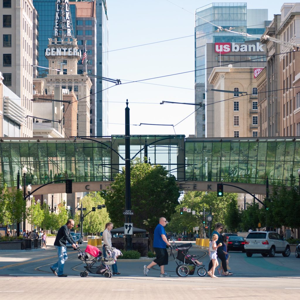 A group of people crossing Main Street at South Temple. The City Creek skybridge, the US Bank building, and the Walker Center building can be seen in the background. 