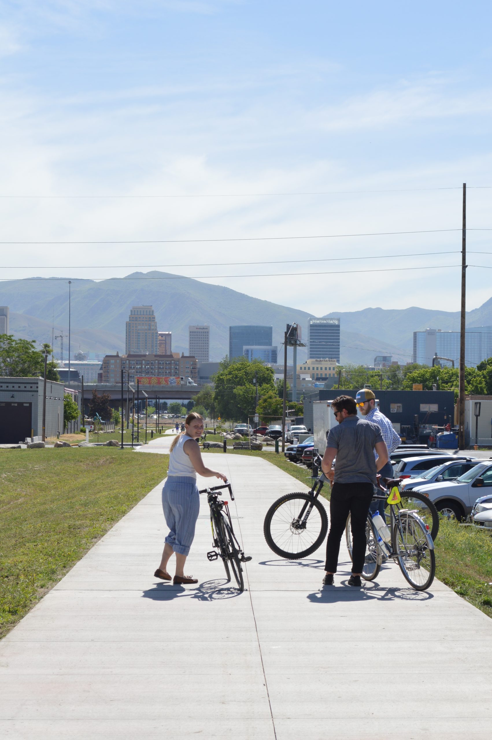 A picture of several people standing on the Folsom Trail with their bicycles. The Salt Lake City skyline is in the background.
