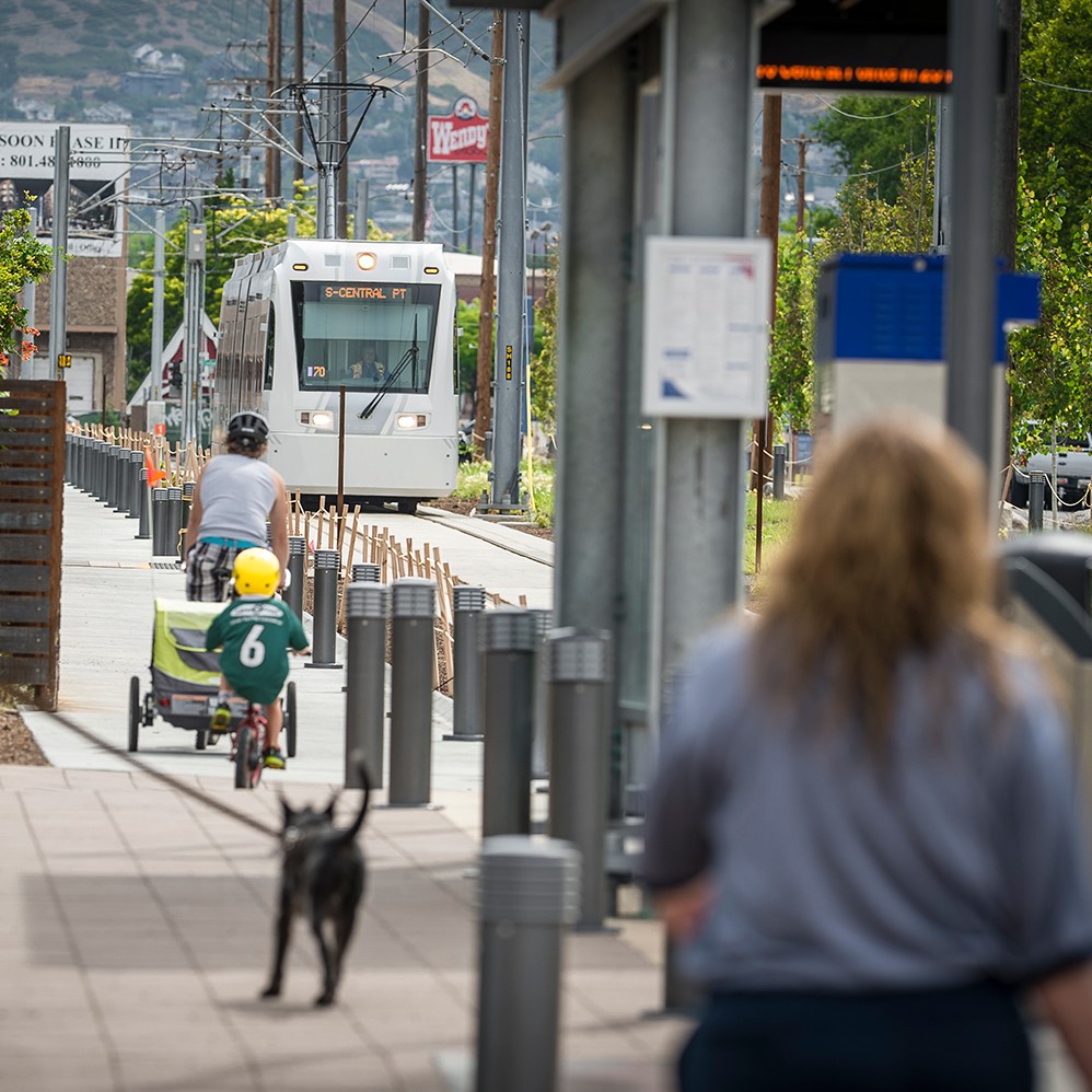 People walking and biking along the S-Line trail while the streetcar passes by.