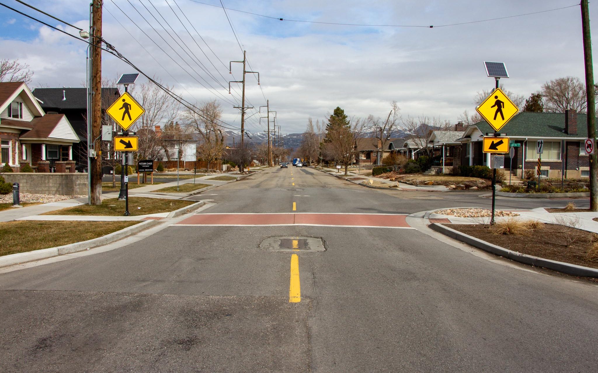 A traffic calming choker on 900 East. The curbs are extended on both sides of the street to shorten the crossing distance for people walking. A red crosswalk and pedestrian activated flashing crosswalk signs improve safety at the crossing. 