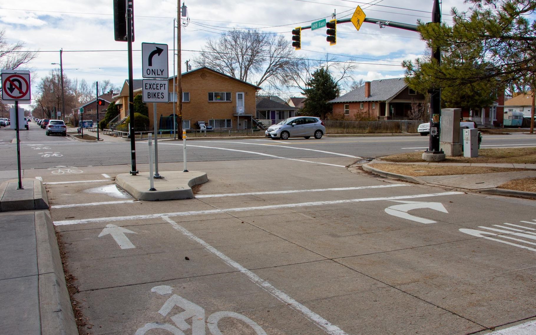 A picture of a forced turn island at the intersection of 1300 South and 600 East at the south end of Liberty Park. The striping and signage notifies drivers that only right turns are allowed. A raised concrete median island provides a safe space for cyclists to wait. On the median island there is a push button to activate the traffic signal for cyclists.