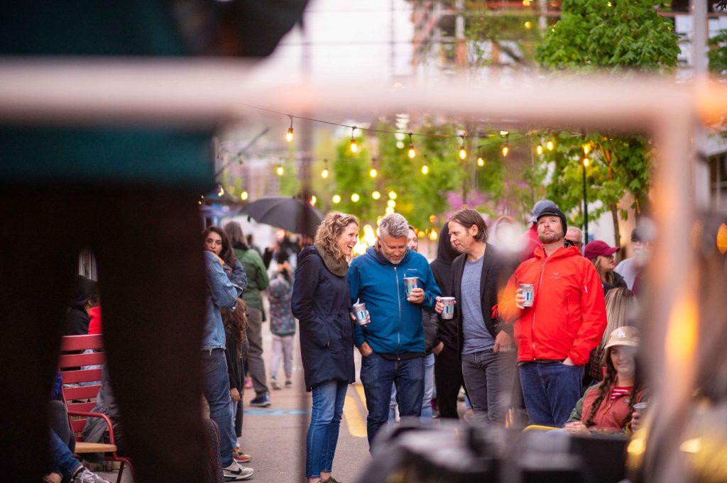 A group of four people in a larger crowd having a conversation and enjoying live music at the Green Loop.