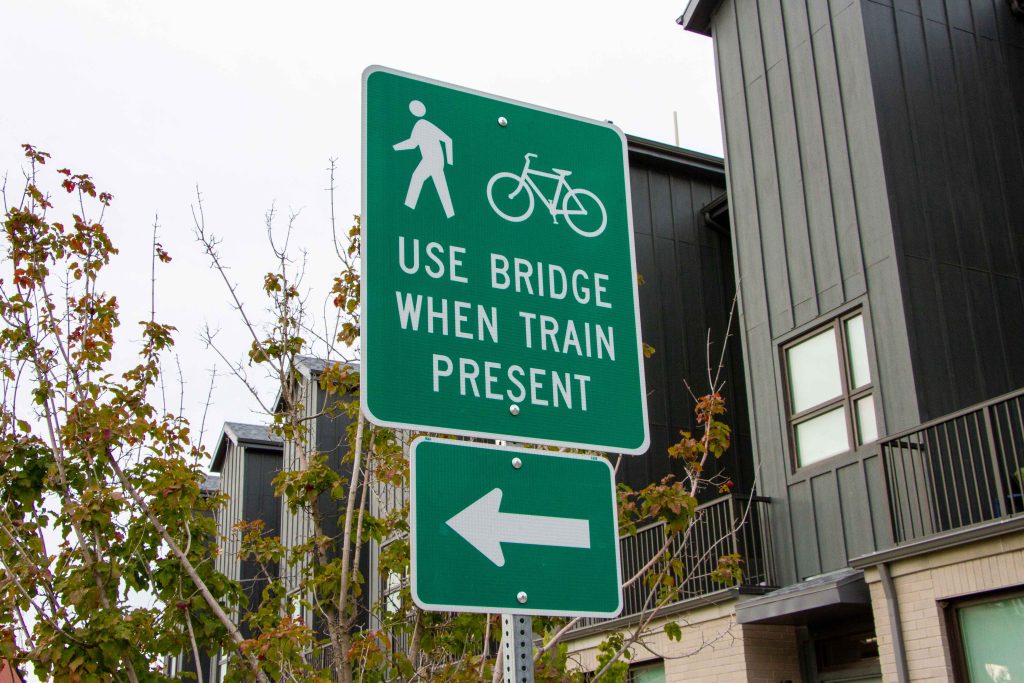 A picture of a green road sign that reads "USE BRIDGE WHEN TRAIN PRESENT" with symbols of pedestrians and cyclists.