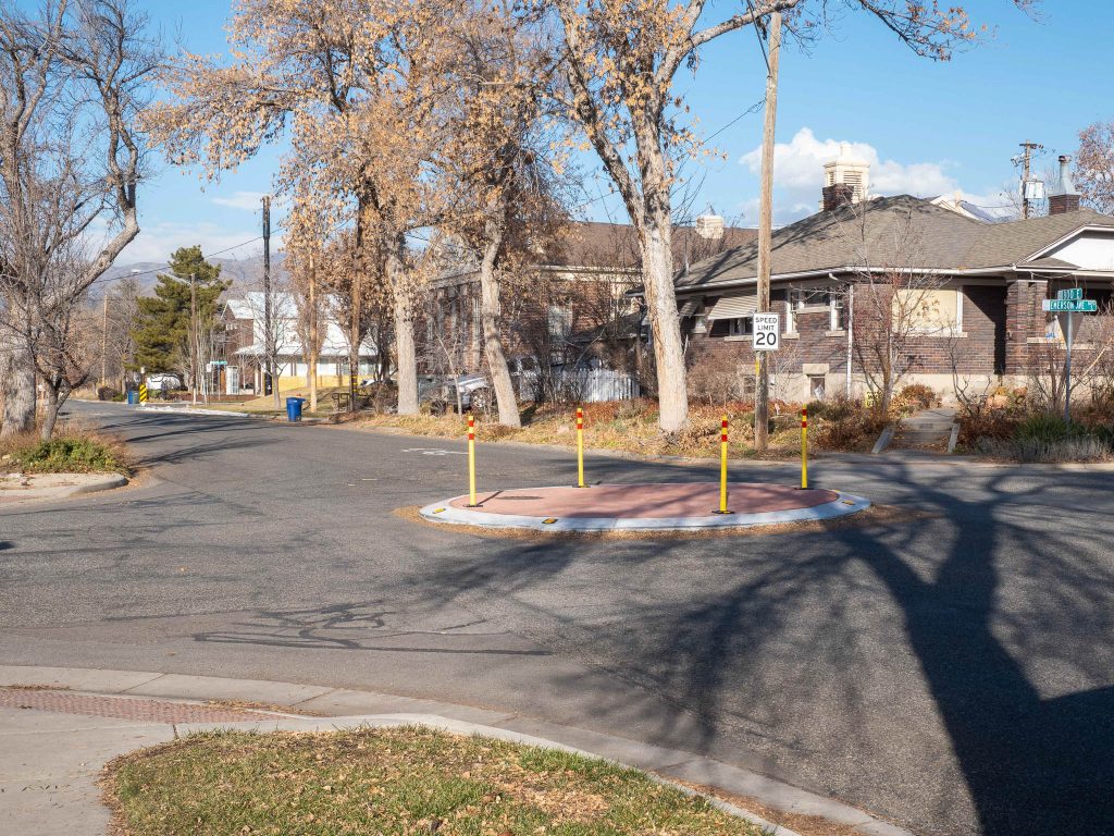A traffic circle on the 800 East Neighborhood Byway. The traffic circle has red stamped brick concrete in the center and bright yellow delineator posts to make it more visible to road users.