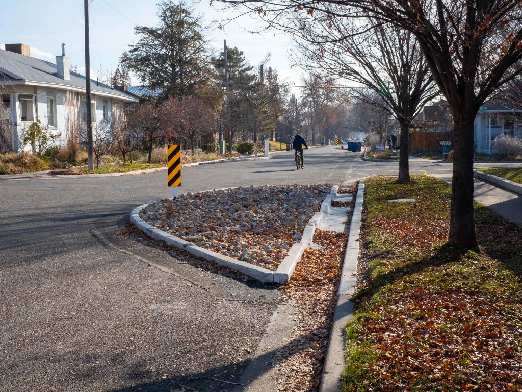 A photo of a curb extension that forms a chicane on the 800 East Neighborhood Byway. A cyclist rides past in the distance.