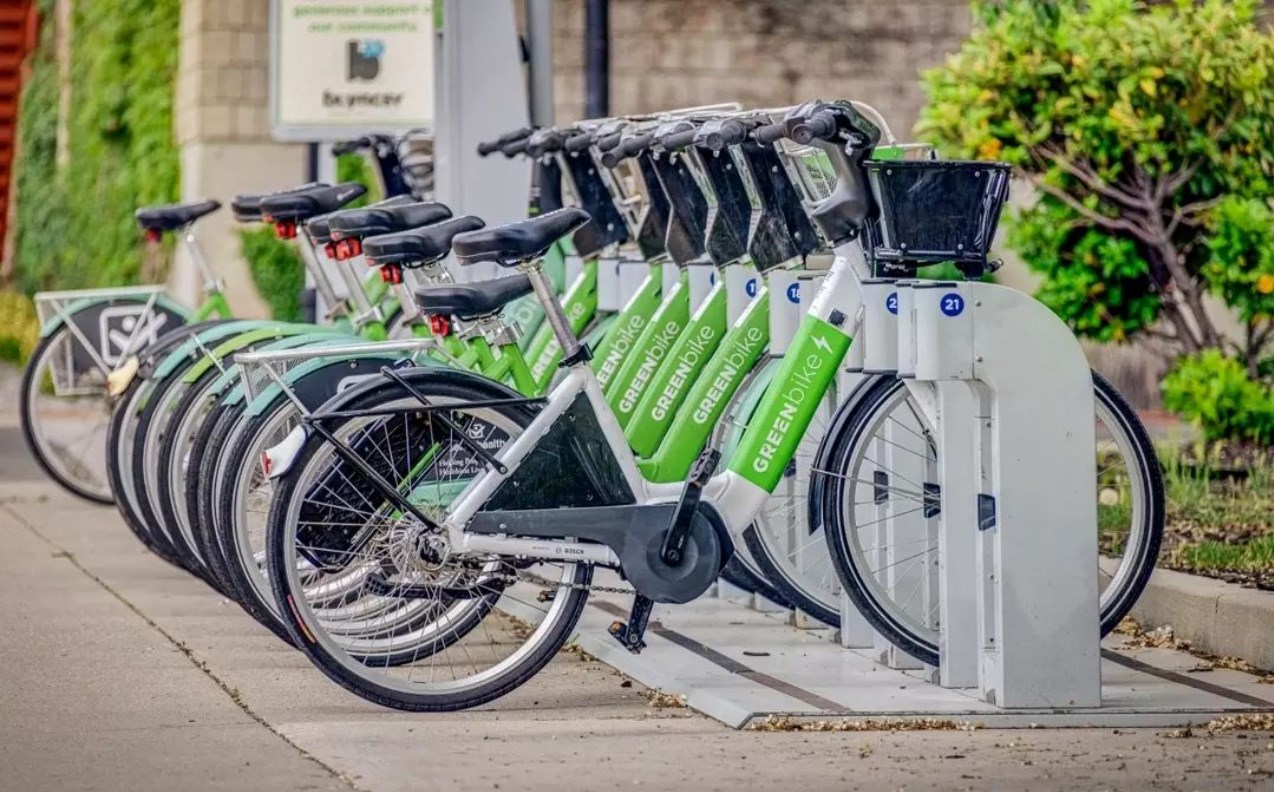The image shows a line of green and white GREENbike electric bicycles neatly docked at a parking station.