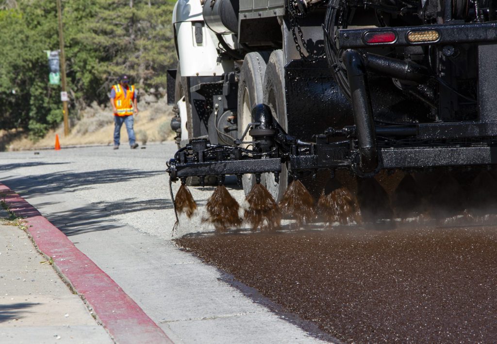 A picture of an oil distributor truck spraying a seal coat onto an asphalt road.