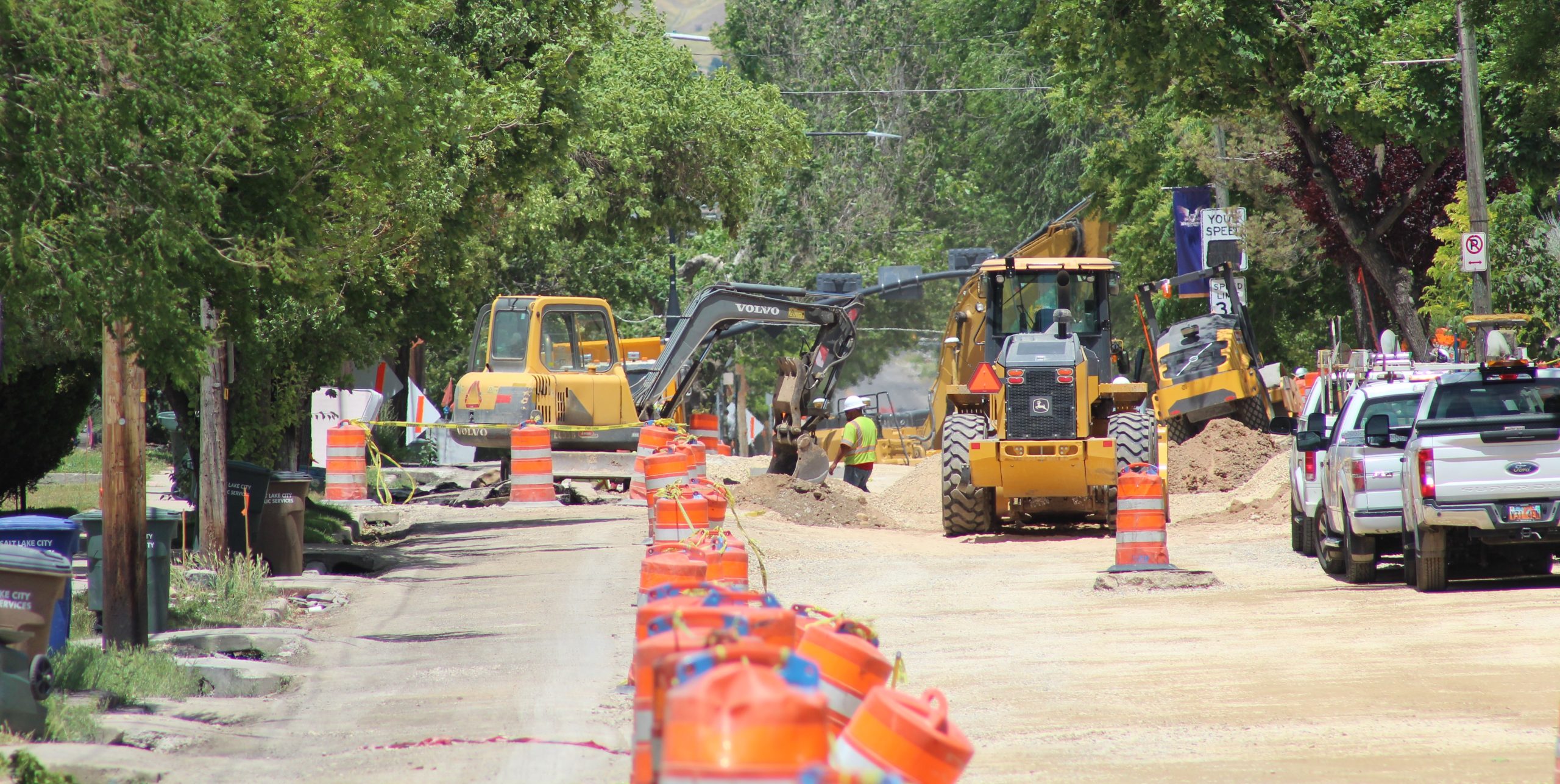 A street construction site with heavy machinery, traffic barrels, and utility vehicles.